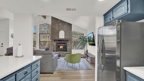 Une cuisine moderne avec une cheminée en pierre, un grand réfrigérateur et un coin salon confortable avec une autre cheminée.