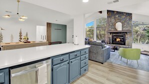 Une cuisine moderne dotée d’un grand îlot central, d’une cheminée en pierre et d’un coin salon confortable offrant une vue sur l’extérieur.