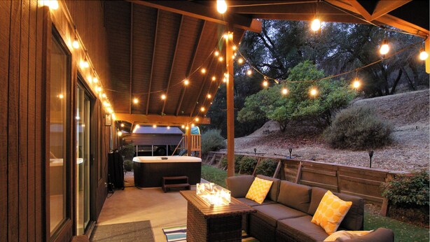 Une terrasse extérieure avec un canapé, une table dotée d’un foyer et des guirlandes lumineuses.