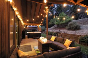 Un patio al aire libre con un sofá, una mesa con una chimenea y luces colgantes.