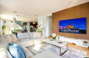 Una sala de estar moderna con un televisor de pantalla plana grande, un sofá blanco, una mesa de centro y una pared de acento de madera.