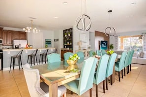 Una cocina moderna con comedor, que cuenta con una mesa de vidrio, sillas color turquesa e iluminación colgante.