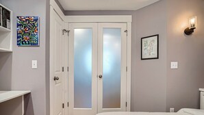 Un dormitorio con cama, armario, estante con libros e iluminación en la pared.