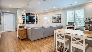 Una cocina moderna con un sofá seccional gris, piso de madera y un comedor con sillas blancas.