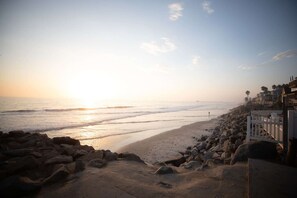 A beach with a rocky shoreline, a white fence, and buildings in the background.