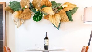 Un área de comedor con una mesa redonda, dos sillas, una botella de vino y un adorno de pared.