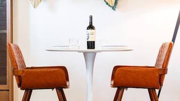 A dining area with a round table, two chairs, a bottle of wine, and a decorative wall piece.