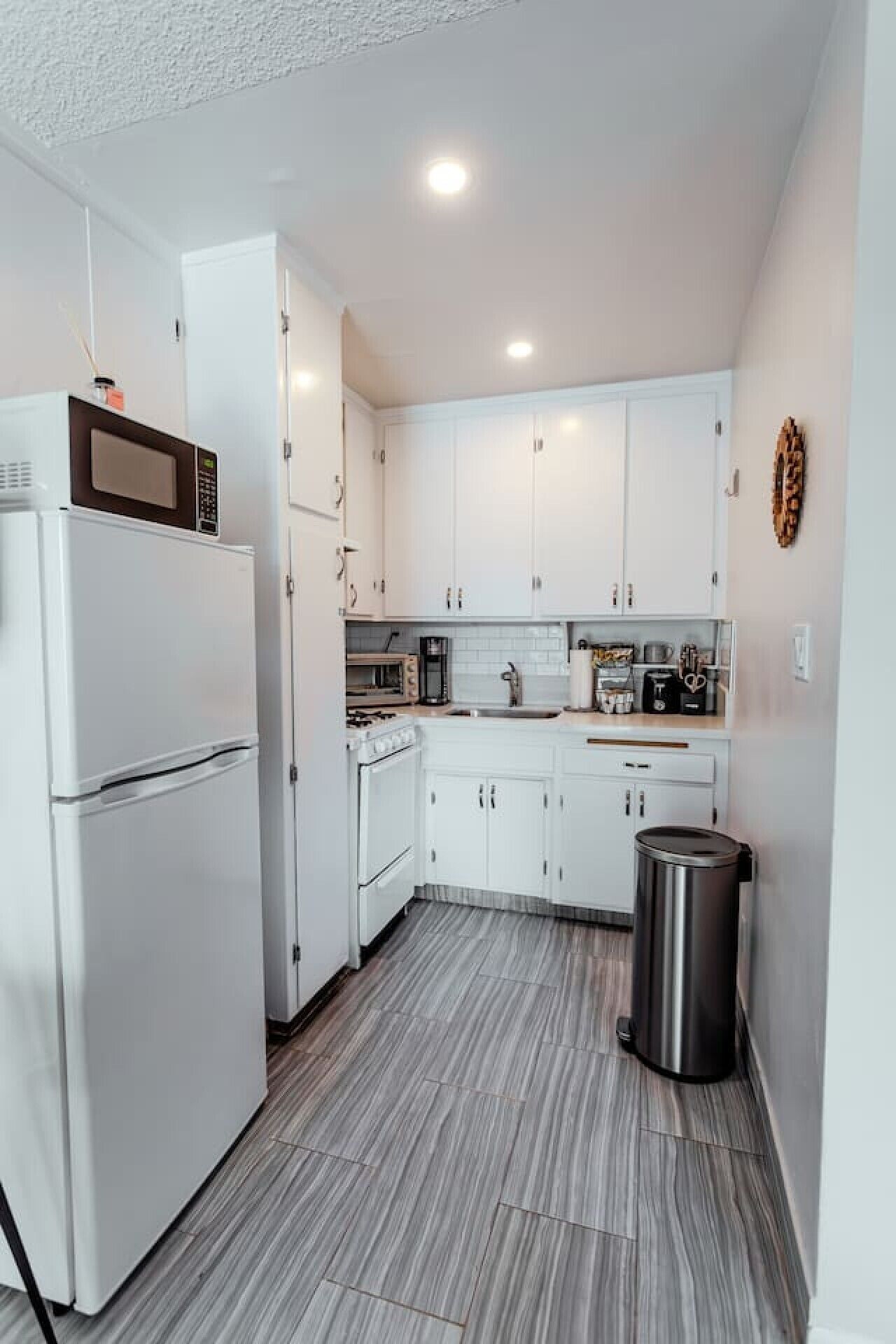 Una cocina compacta con gabinetes blancos, microondas integrado, estufa y un cesto de basura.