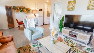 A living room with a sofa, armchair, coffee table, TV, and decorative plants.