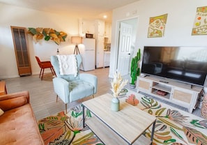 A living room with a sofa, armchair, coffee table, TV, and decorative plants.
