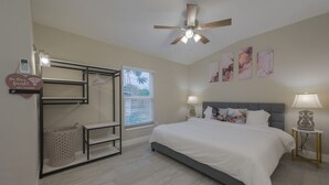 Ein Schlafzimmer mit Bett, Deckenventilator, Fenster mit Jalousien, einer Wandablage und einem an der Wand befestigten Telefon.