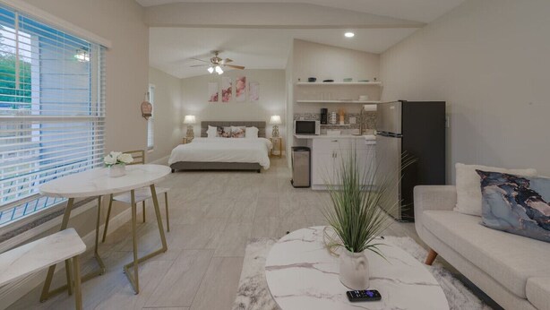 Eine moderne Wohnung mit Schlafzimmer, Wohnzimmer und Küche. Sie verfügt über ein Bett, einen Esstisch, ein Sofa und eine Küchenzeile mit Kühlschrank und Mikrowelle.