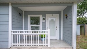Ein Haus mit weißem Veranda, einer Tür mit der Nummer 5 und einer Fußmatte mit dem Schriftzug 'Stay awhile'.