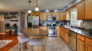 A kitchen with wooden cabinets, a granite countertop, stainless steel appliances, and a bar area with stools. - Beautiful Spacious Well-Stocked Home in Downtown Rangeley. Pet & Family Friendly (Rangeley)