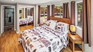 Ein geräumiges Schlafzimmer mit einem großen Bett, Holzboden und Blick ins Freie durch große Fenster.