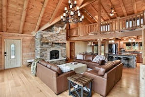 A spacious living area with a stone fireplace, leather sofas, a wooden ceiling, and a kitchen area with a bar.