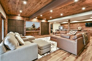 A spacious living room with a large couch, a coffee table, and a television mounted on a wooden wall.