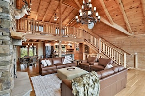 A spacious living area with a large sofa, a fireplace, a stone wall, and a staircase leading to an upper level.