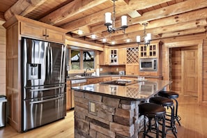 A kitchen with a large island, stainless steel appliances, wooden cabinets, and a stone accent wall.