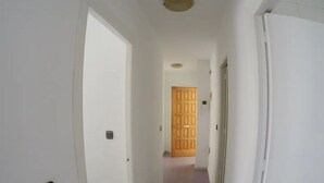 A narrow hallway with white walls, a wooden door at the end, and a purple-tiled floor. - Beachfront apartment (La Cala del Moral)