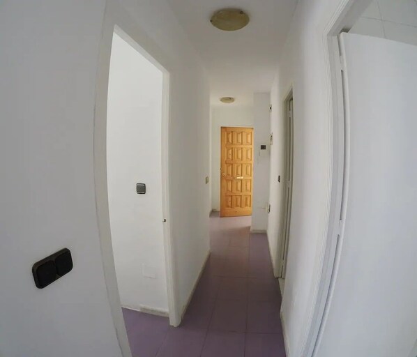A narrow hallway with white walls, a wooden door at the end, and a purple-tiled floor.
