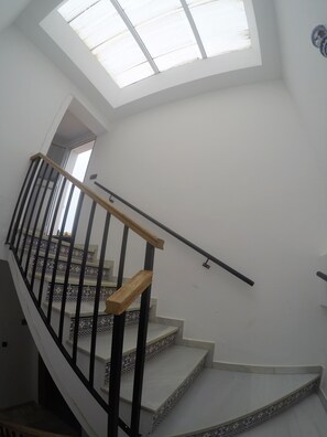 Un escalier avec une rampe en bois et des balustres noires, menant à une pièce dotée d’une lucarne.