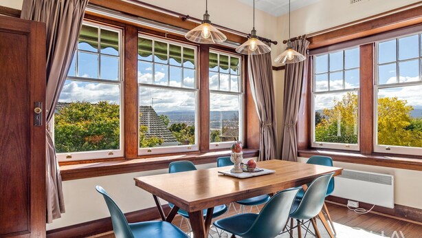 Un coin repas avec une table en bois, des chaises bleues et de grandes fenêtres avec des rideaux.