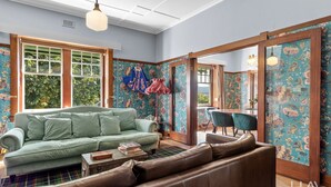 Une pièce avec un canapé vert, un divan en cuir marron, une table à manger avec des chaises et un papier peint à motifs floraux.