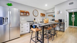 Eine moderne Küche mit einem Edelstahl-Kühlschrank, Holzschränken, einer zentralen Kochinsel mit Barhocker und einer grünen Wandgestaltung.