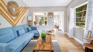 Ein modernes Wohnzimmer mit einem blauen Sofa, einem Holztisch und einem großen Fenster mit gemusterten Vorhängen.