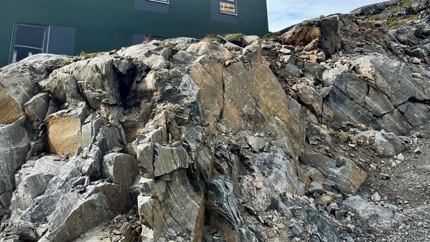 A modern building with a flat roof and multiple windows, situated on rocky terrain.