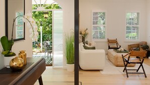 A modern living room with a sofa, chairs, a coffee table, and a dining table. There is a large window with blinds, a door leading to a patio, and a mirror on the wall. - Sweet Juliet, Double Bay (Double Bay)