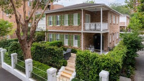 A two-story brick house with green shutters, a balcony with white railings, and a small front porch with a table and chairs. - Sweet Juliet, Double Bay (Double Bay)