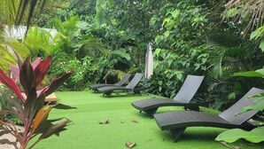 A garden with artificial grass, several lounge chairs, and tropical plants. - One Life Villas (Tamarindo)