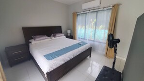 A bedroom with a bed, bedside tables, a standing fan, and a window with curtains. - One Life Villas (Tamarindo)