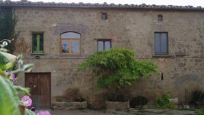 Un edificio de piedra rústico con un pequeño jardín, una puerta de madera y un ventanal con marco verde.
