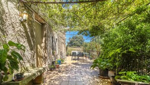 Un estrecho patio con un banco de piedra, plantas en macetas y una mesa con sillas.