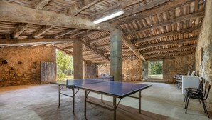 Un espacio interior amplio con mesa de ping pong, paredes de piedra y un techo alto de madera.