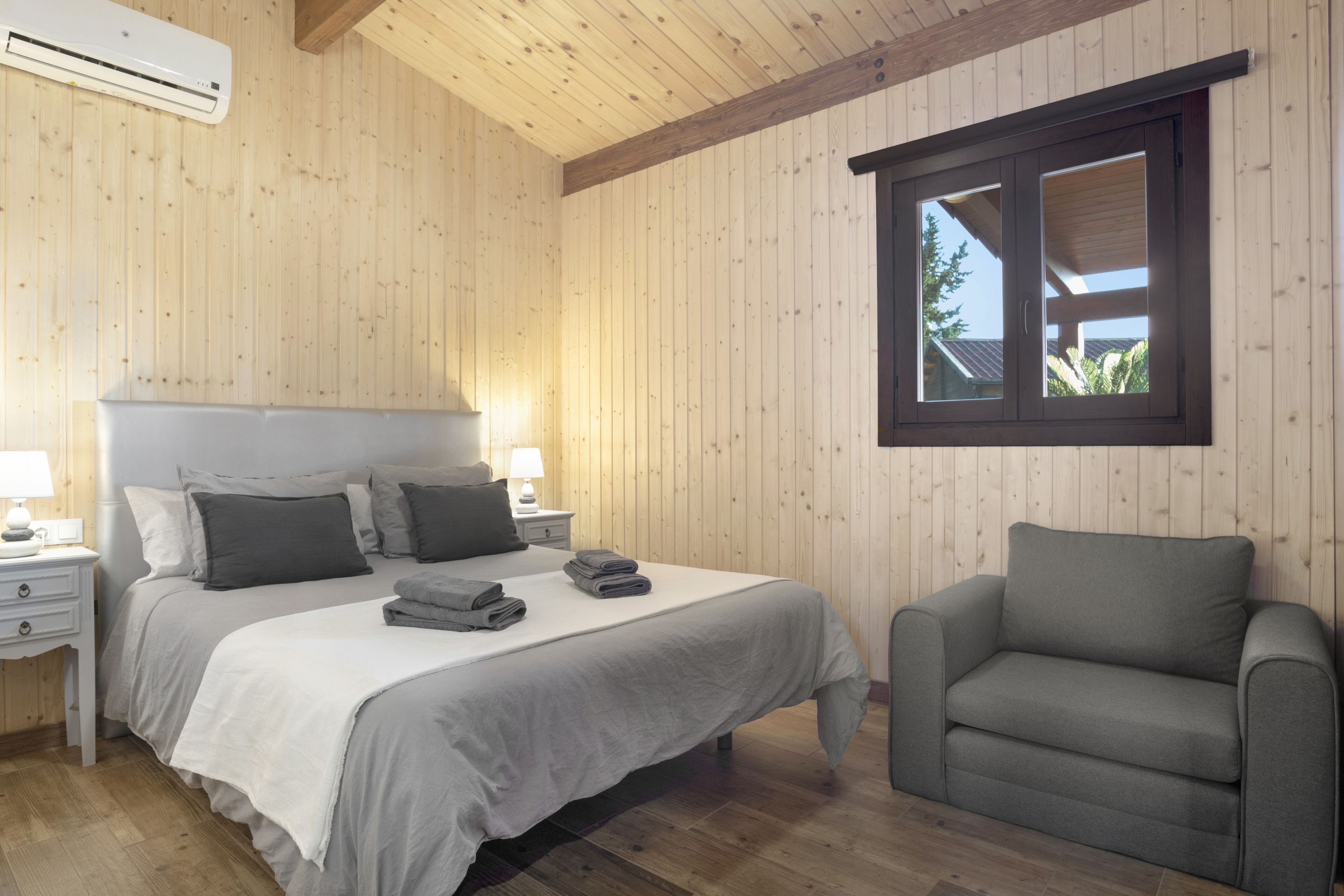 Quarto com cama, cadeira, janela e paredes de madeira.
