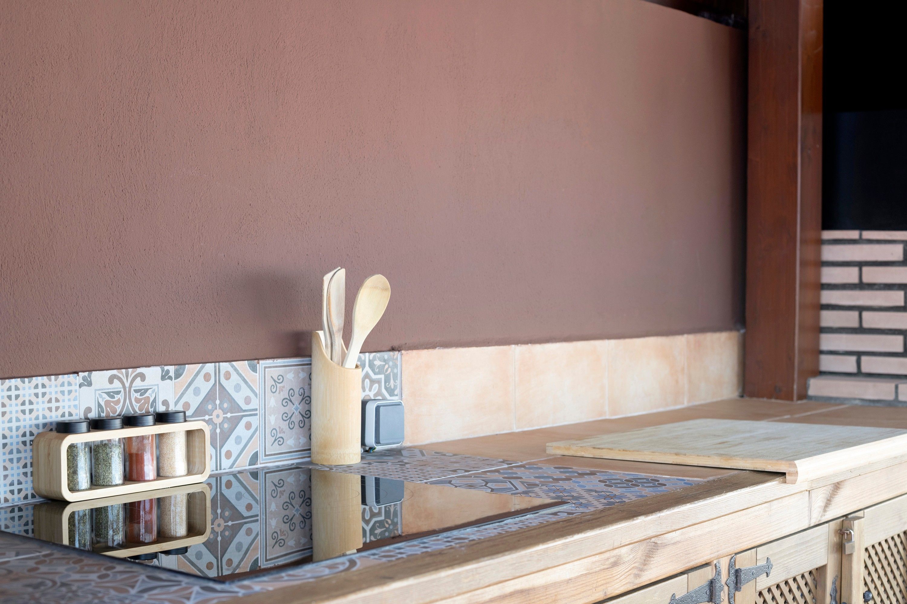 Una encimera de cocina con un estante de madera para especias, un recipiente de madera para utensilios y un salpicadero azulejado.