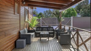 A covered outdoor patio with wooden flooring, wicker furniture, and a view of the surrounding area.