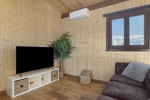 A living room with a flat-screen TV on a white stand, a large potted plant, a brown sofa, and a window with a view of the sky. - Villa 'Fatema' with Private Pool, Wi-Fi, and Air Conditioning (Conil de la Frontera)