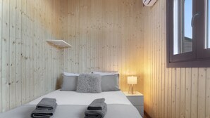 A wooden-paneled room with a bed, pillows, a nightstand, and a window.
