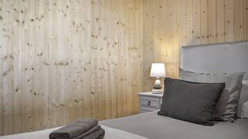 Une chambre d’hôtel avec un mur en bois, un lit avec une literie grise, une table de chevet avec une lampe et une serviette grise pliée.