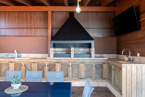An outdoor kitchen area with a built-in grill, a dining table with chairs, and a TV mounted on the wall. - Villa 'Fatema' with Private Pool, Wi-Fi, and Air Conditioning (Conil de la Frontera)
