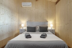 A bedroom with a wooden paneled wall, a bed with grey bedding, two bedside lamps, and a wall-mounted air conditioner. - Villa 'Fatema' with Private Pool, Wi-Fi, and Air Conditioning (Conil de la Frontera)
