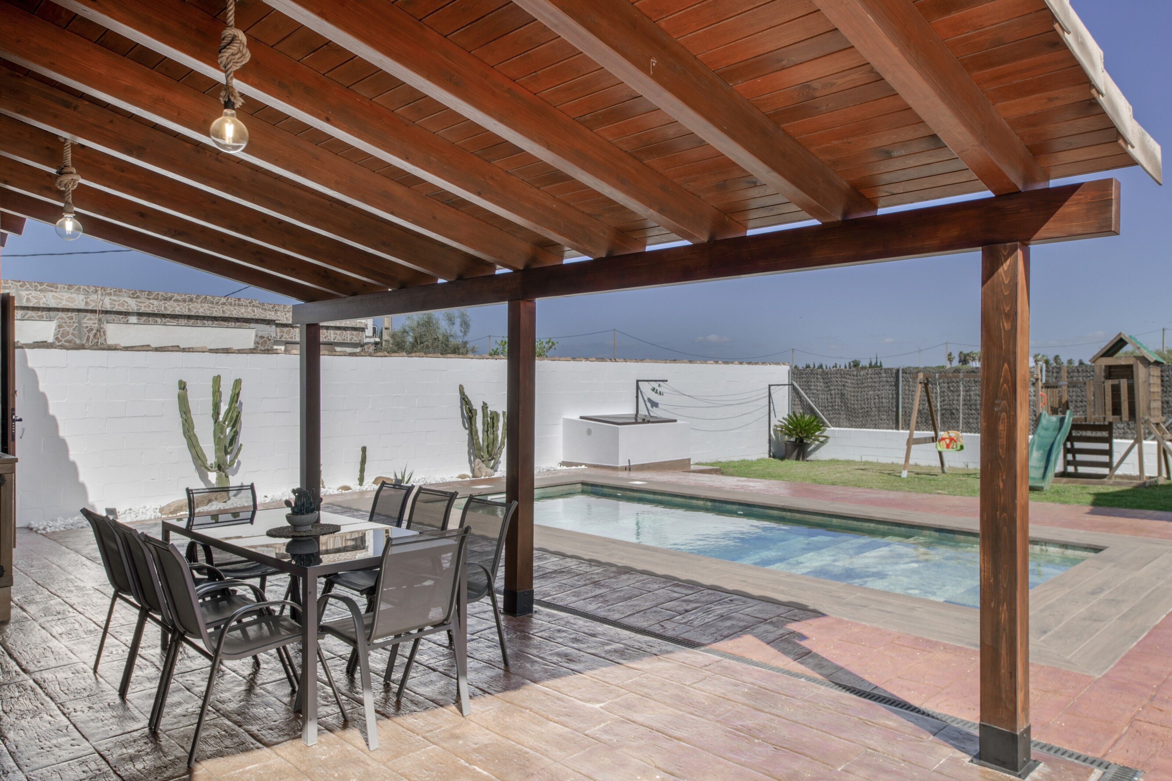 A covered patio with a pool, outdoor seating, and a view of the backyard.