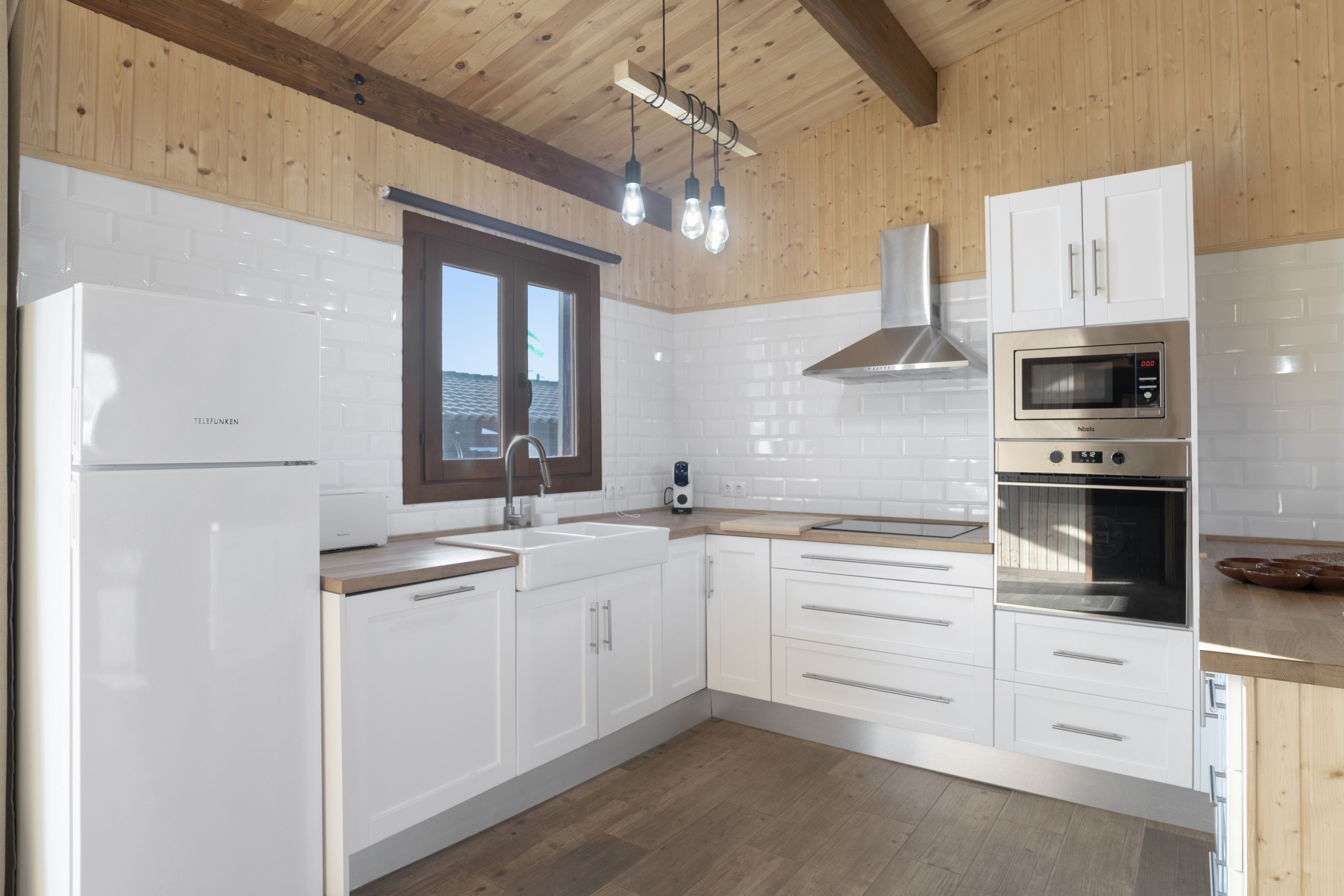 Une cuisine moderne avec des meubles blancs, des appareils en acier inoxydable et un plafond en bois.