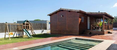 Una piscina con muelle de madera, una estructura de juegos de madera y un pequeño edificio de madera.