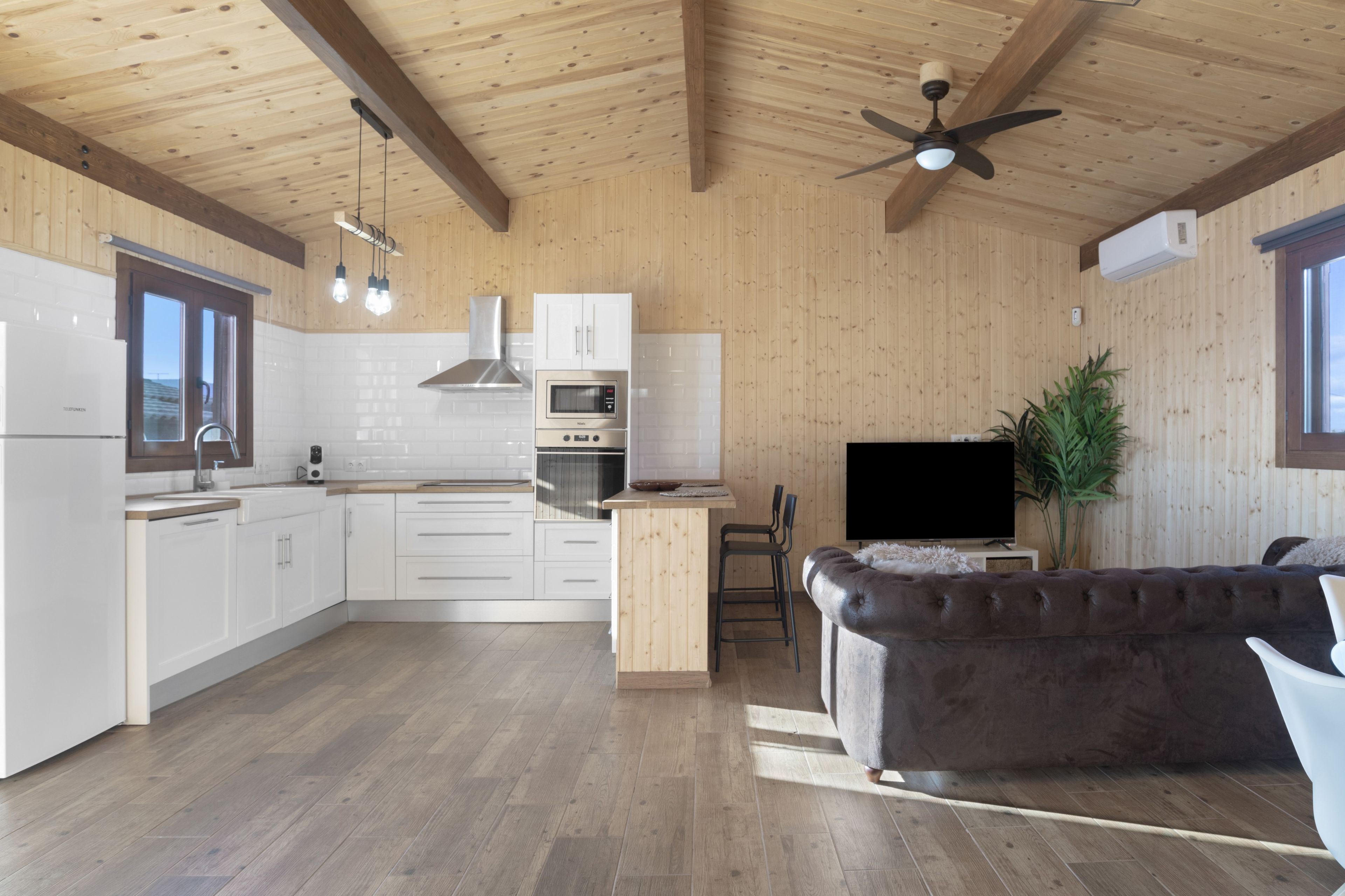 Una cocina moderna con armarios blancos, horno integrado y ventilador de techo.